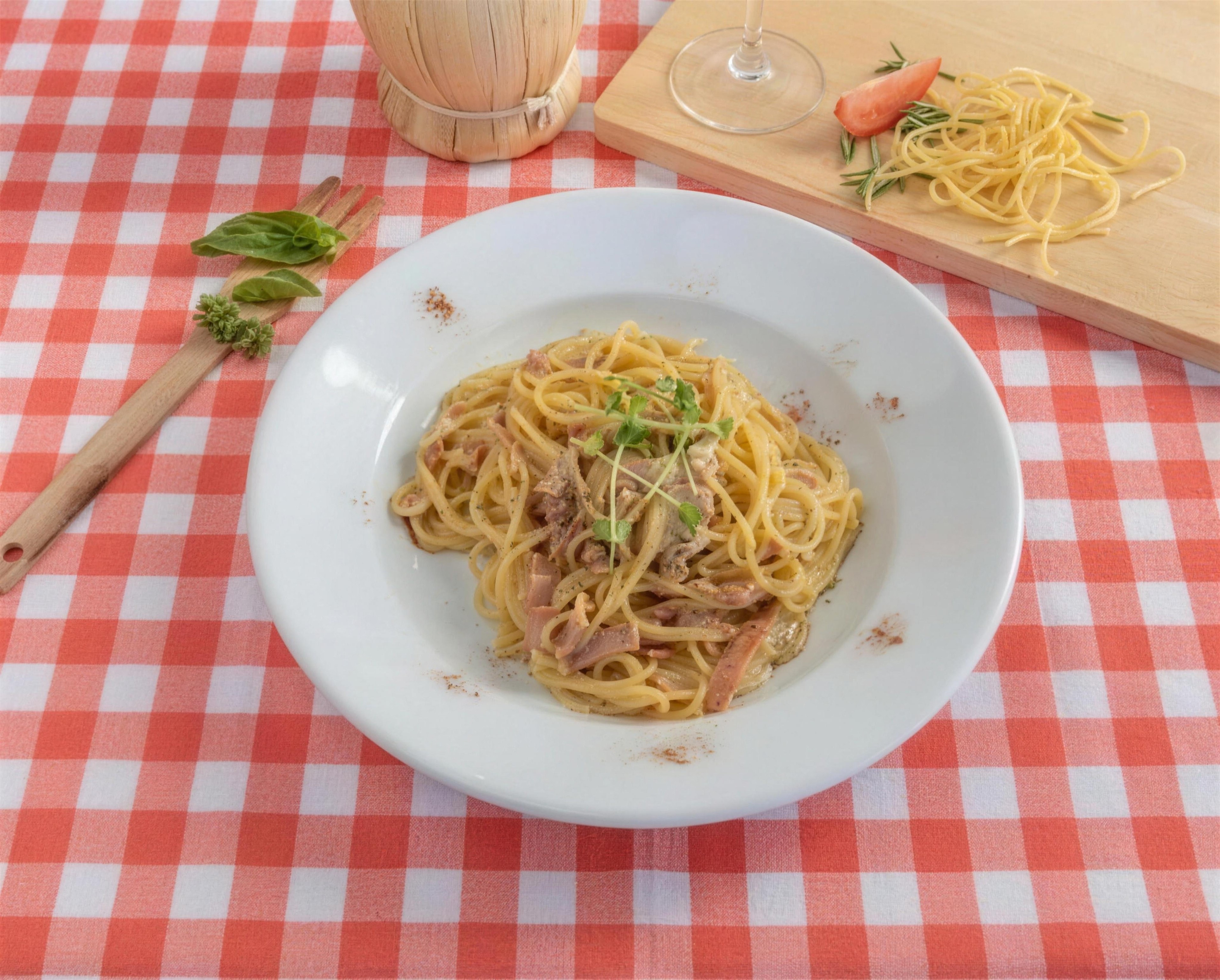 Spaghetti Carbonara with bacon in a white bowl on a red gingham tablecloth