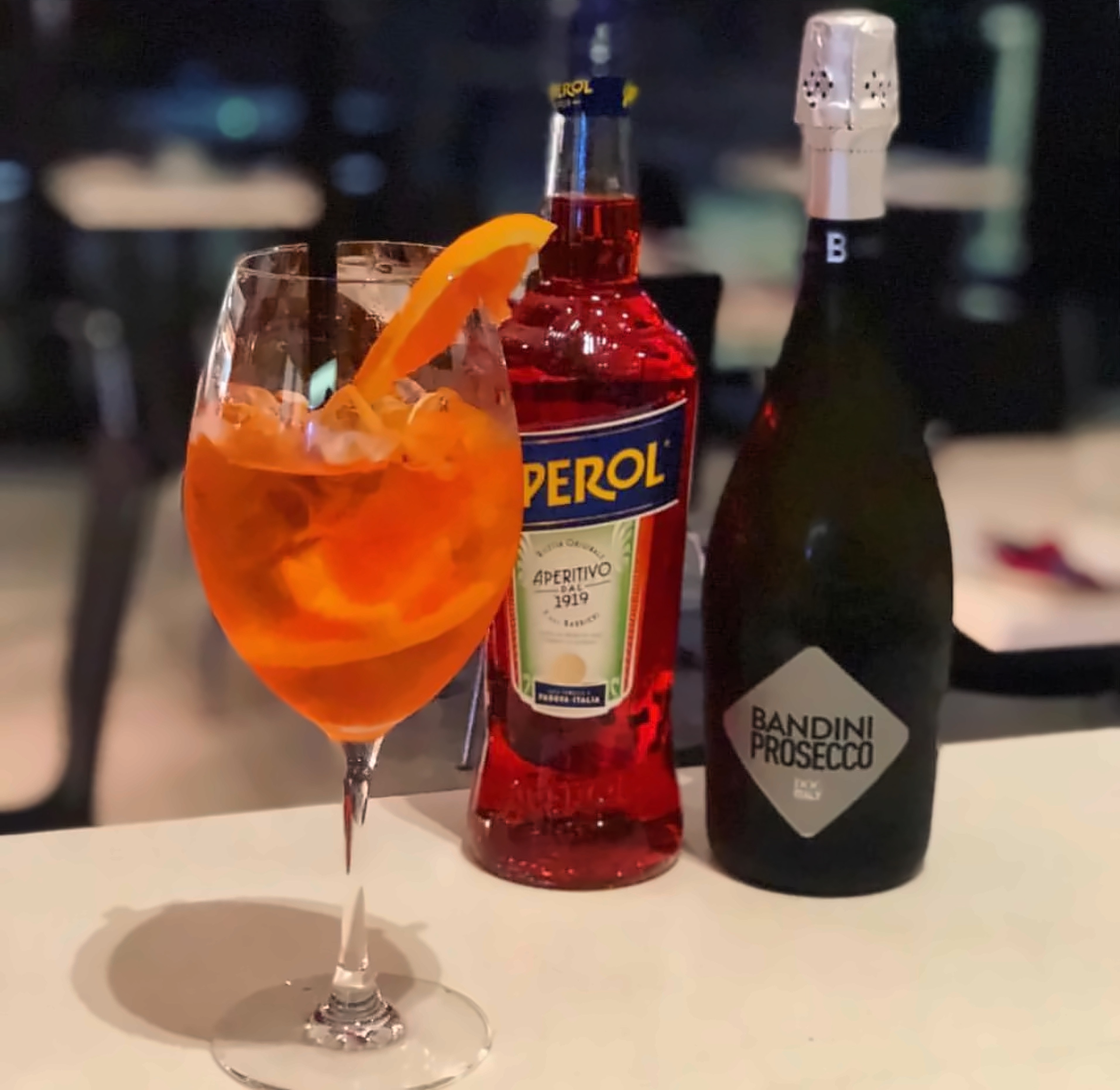 An Aperol Spritz with an orange slice beside bottles of Aperol and Prosecco on the Sorano bar