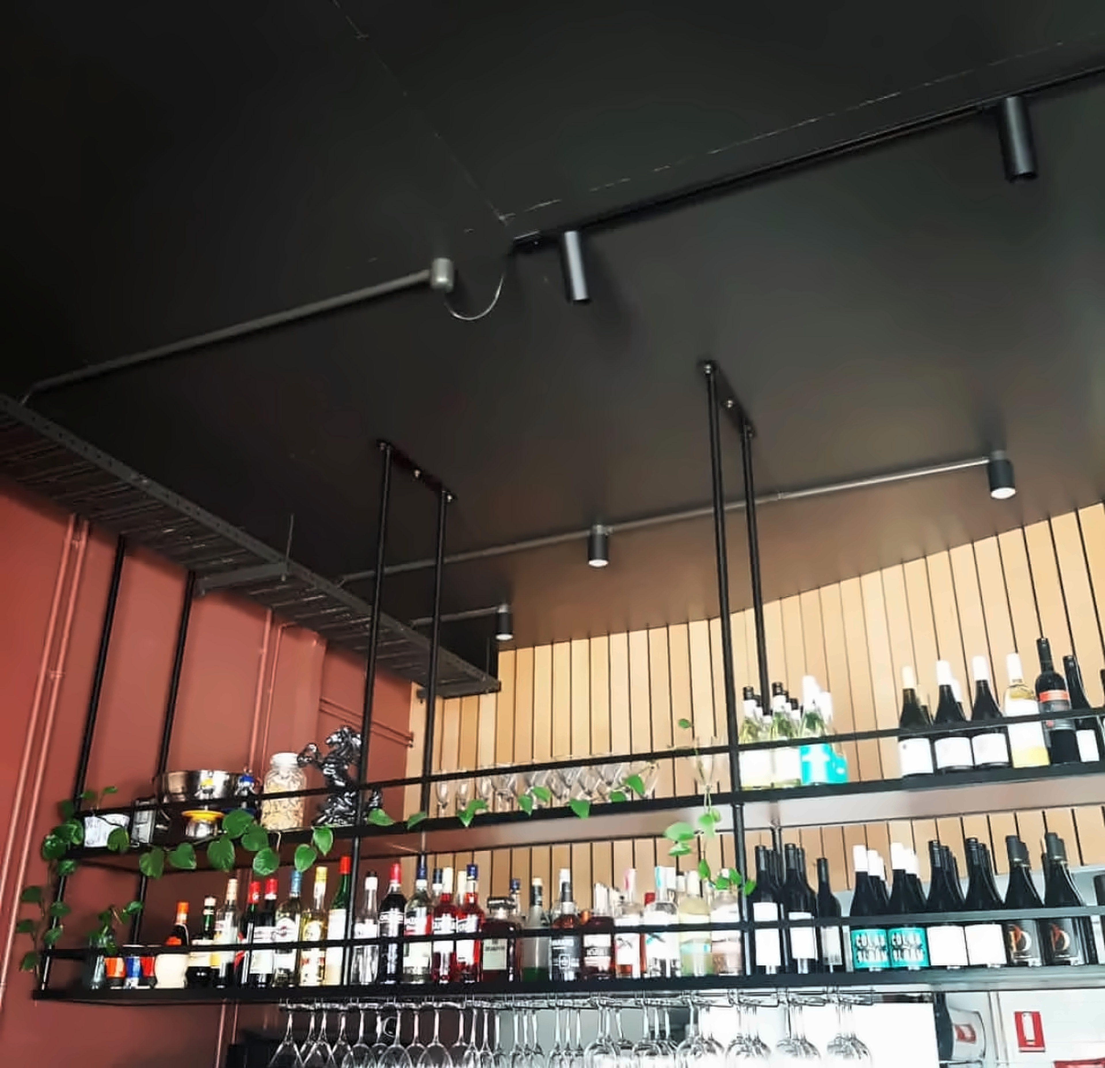 The Sorano bar: floating black shelves of wine and spirits, hanging glasses, a timber slat wall and a terracotta wall with trailing plants